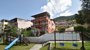 A playground with a slide and swings, surrounded by buildings and a hillside. - Duygu Pension (Fethiye)