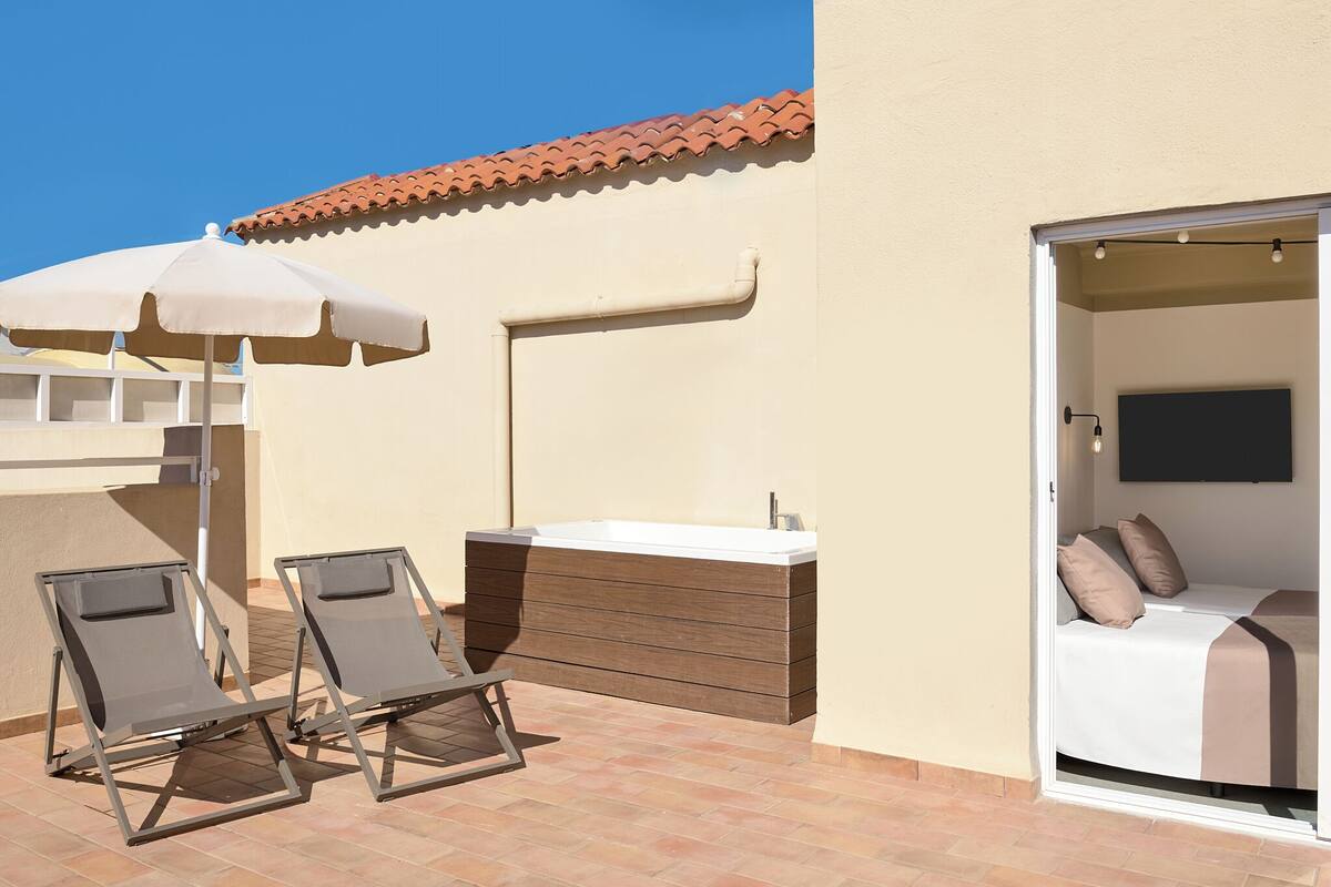 A balcony with two lounge chairs, a white umbrella, and a small sink.