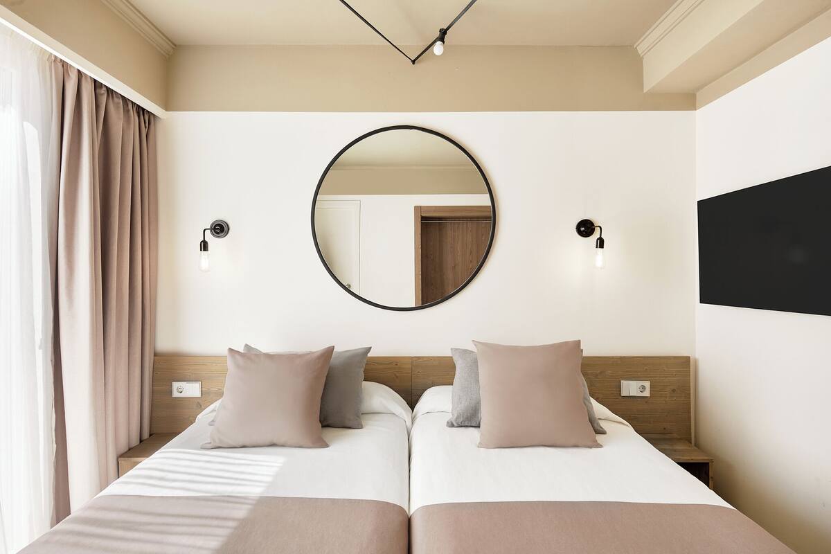 A double bed with a wooden headboard, two bedside tables, and a round mirror on the wall.