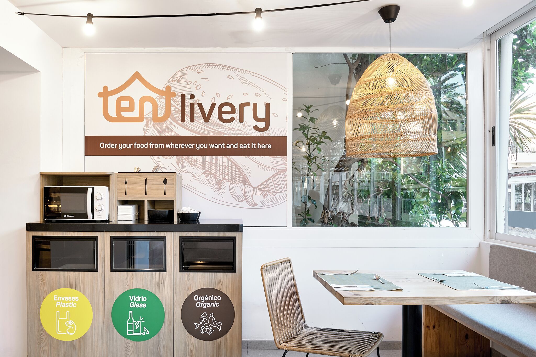 A modern kitchen area with a microwave, a sink, and a wooden cabinet with recycling bins labeled "Envases Plastic," "Vidrio Glass," and "Organico Organic."