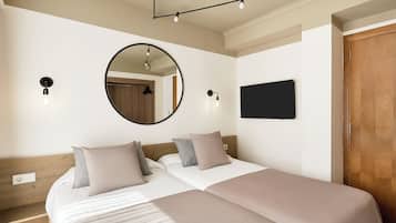 A hotel room with two beds, a round mirror, wall-mounted lights, a flat-screen TV, and a wooden door.