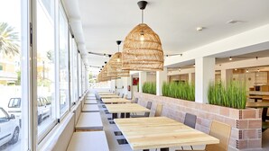 A restaurant with long tables and chairs, large windows, and hanging wicker lamps. - tent Capi Playa (Palma de Mallorca)