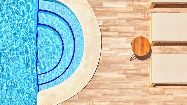 A swimming pool with a tiled edge, wooden flooring, and a wooden table with chairs. - tent Capi Playa (Palma de Mallorca)