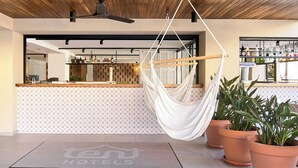A modern hotel lobby with a wooden ceiling, a hanging hammock, a reception desk, and a bar area. - tent Capi Playa (Palma de Mallorca)