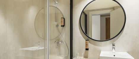 A modern bathroom with a glass-enclosed shower, a white sink, and a round mirror.