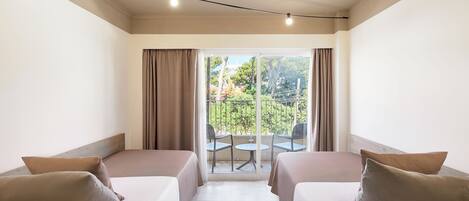 A hotel room with two beds, a balcony with a table and chairs, and a view of greenery.