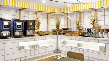 Un café moderne avec un décor épuré, un mur recouvert de carreaux, des machines à café et des sièges disposés avec soin.