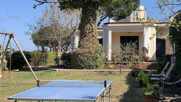 Enjoy a game of ping pong in a serene garden setting surrounded by lush greenery and a classic building.