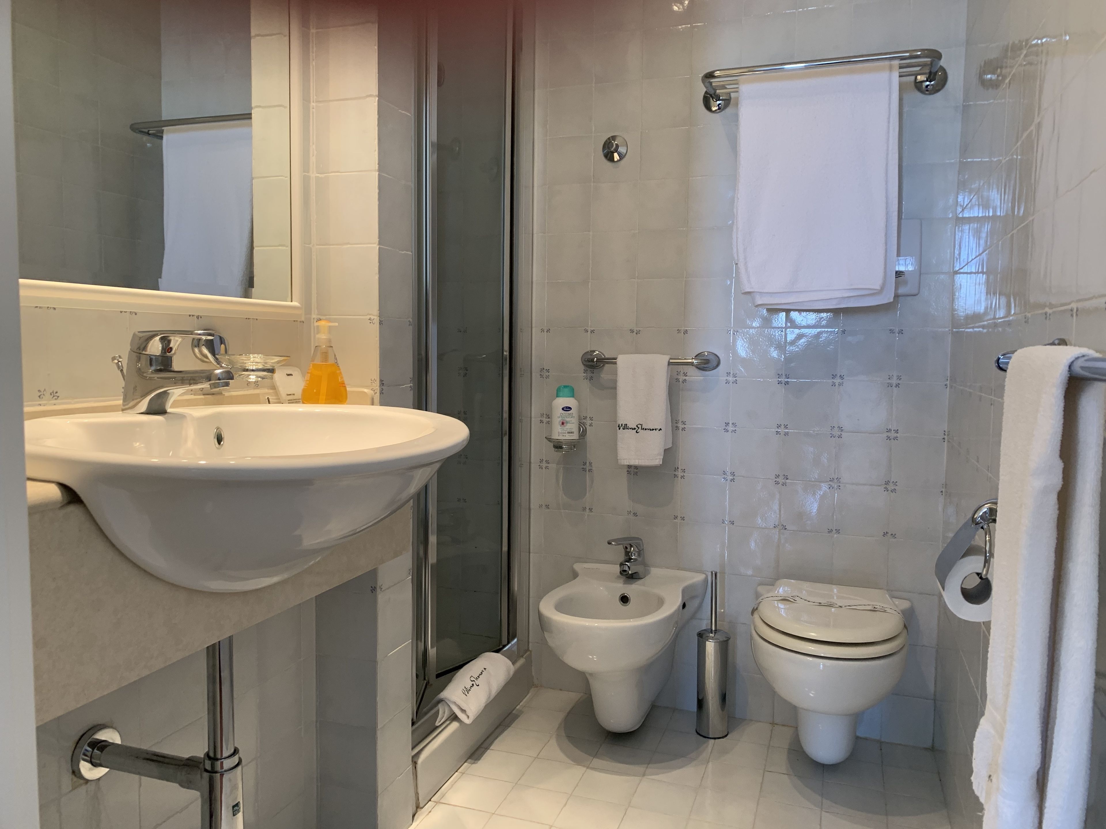 A modern bathroom with a sink, bidet, toilet, and a glass shower enclosure.