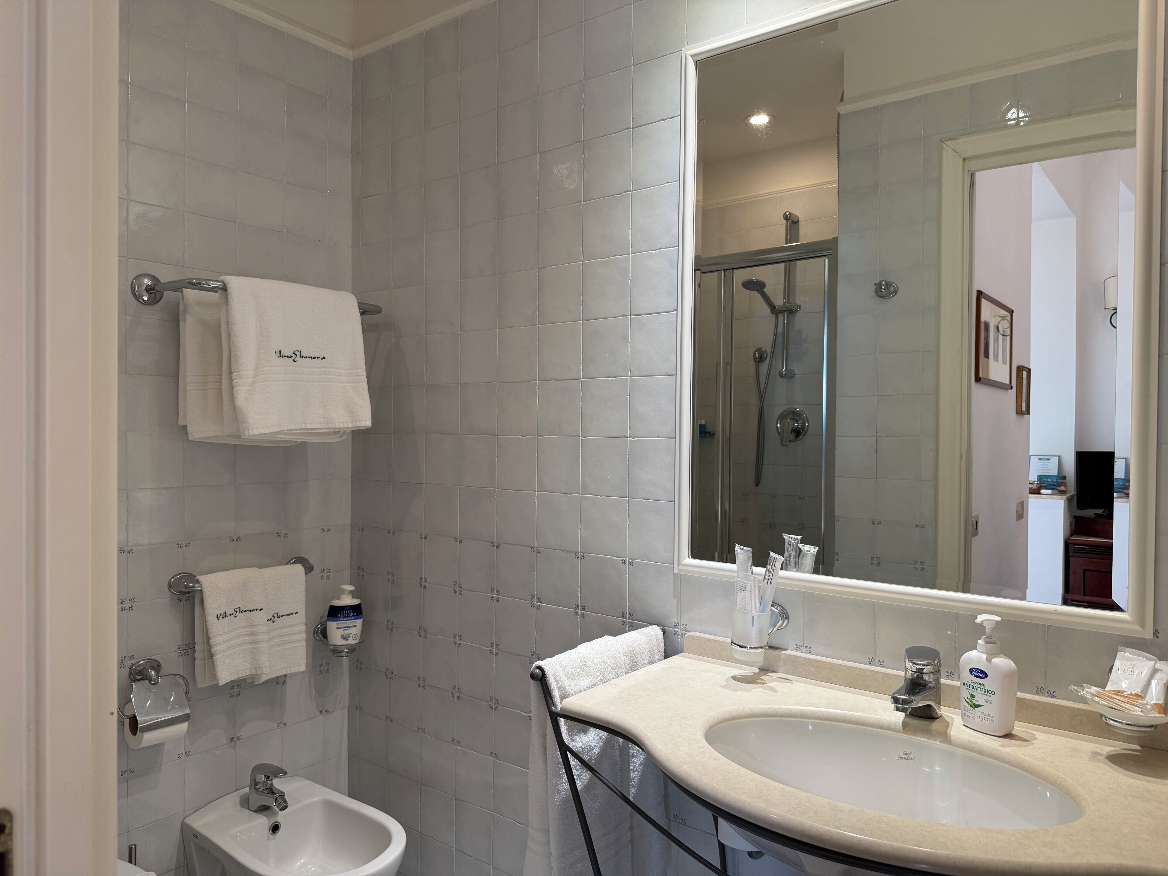 Un baño moderno con un espejo grande, un lavamanos, un bidé y una ducha.