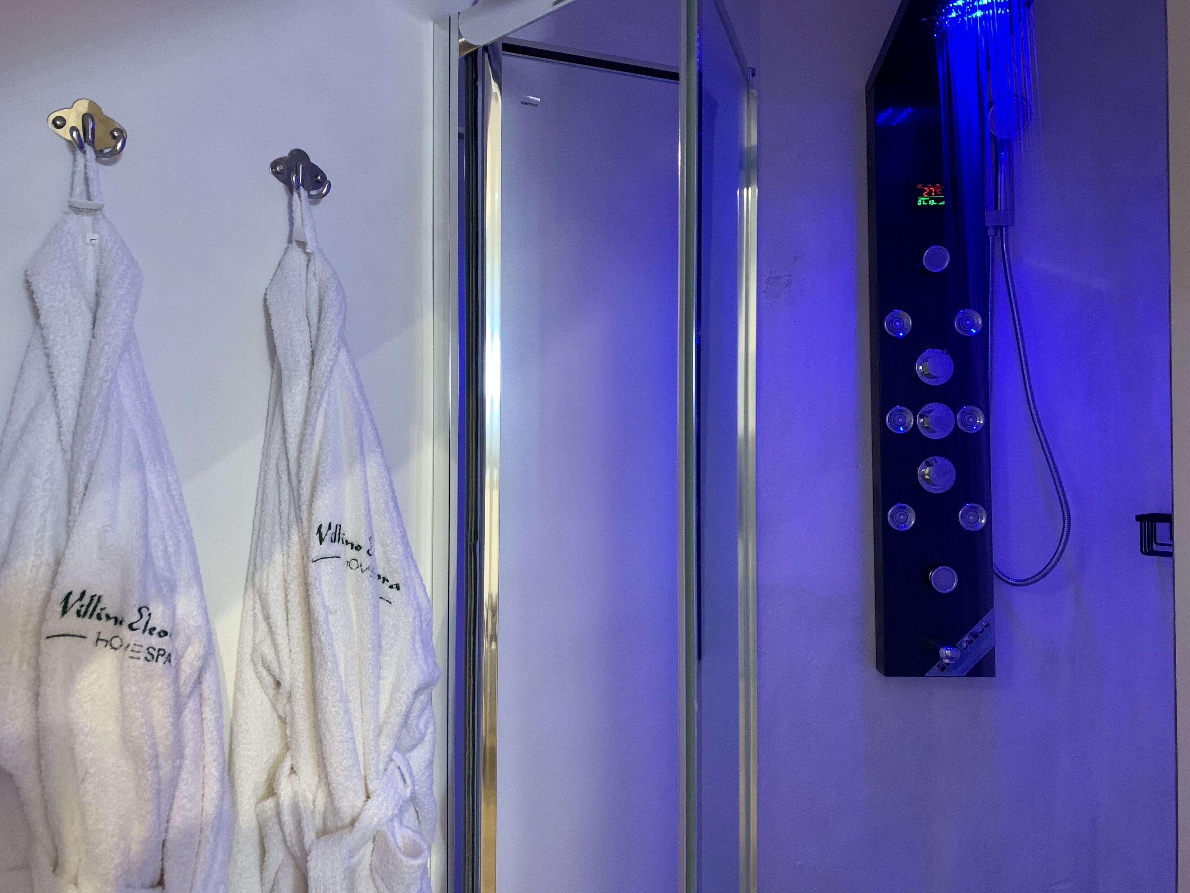 Un baño con dos toallas colgadas en ganchos, un box de ducha de vidrio y un panel de control con varios botones y una pantalla digital.