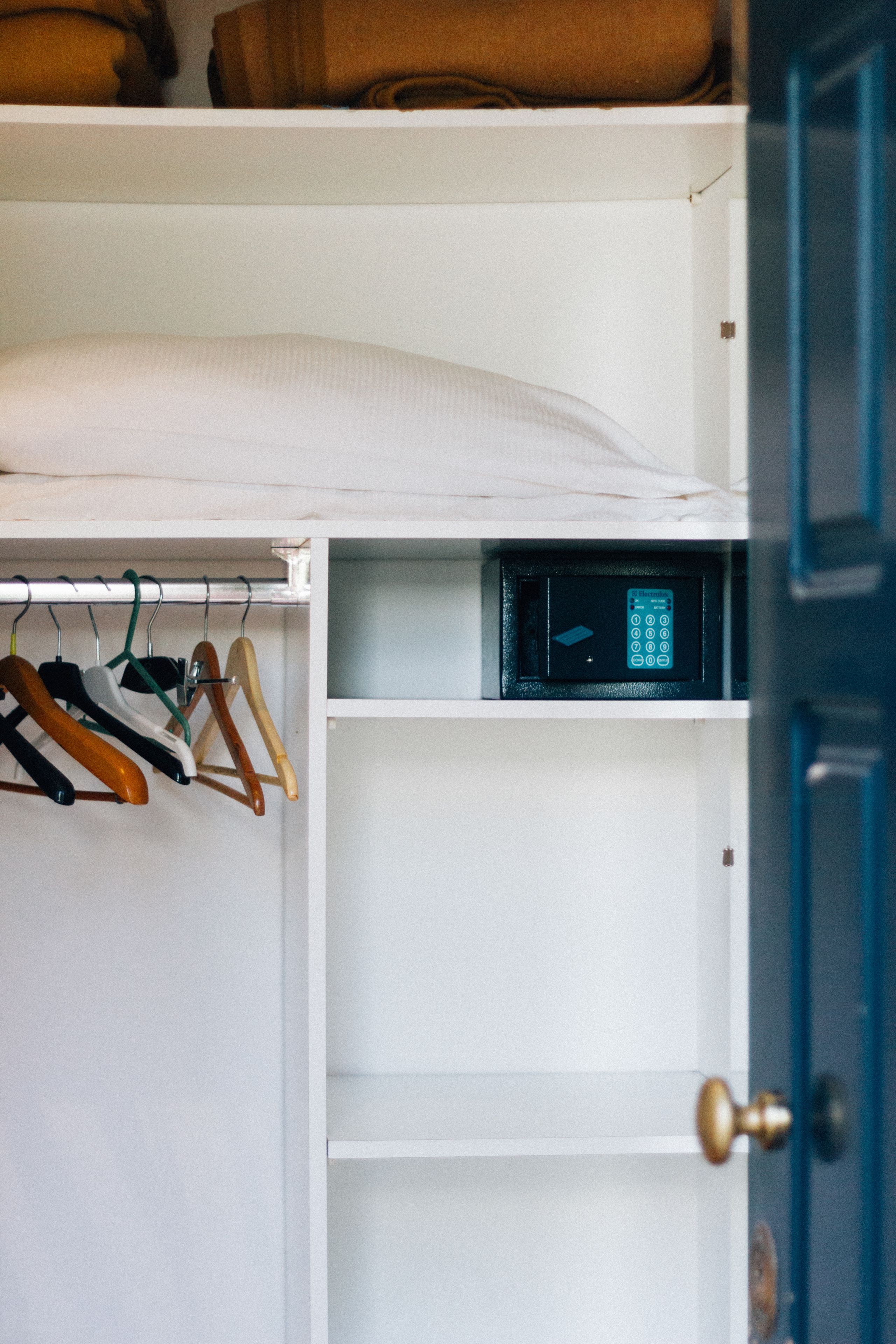 A wardrobe with hanging clothes, a shelf with a microwave, and a door with a brass handle.
