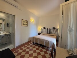 Habitación de hotel con piso a cuadros, cama con cabecera, mesita de noche y espejo, con una lámpara fijada a la pared.
