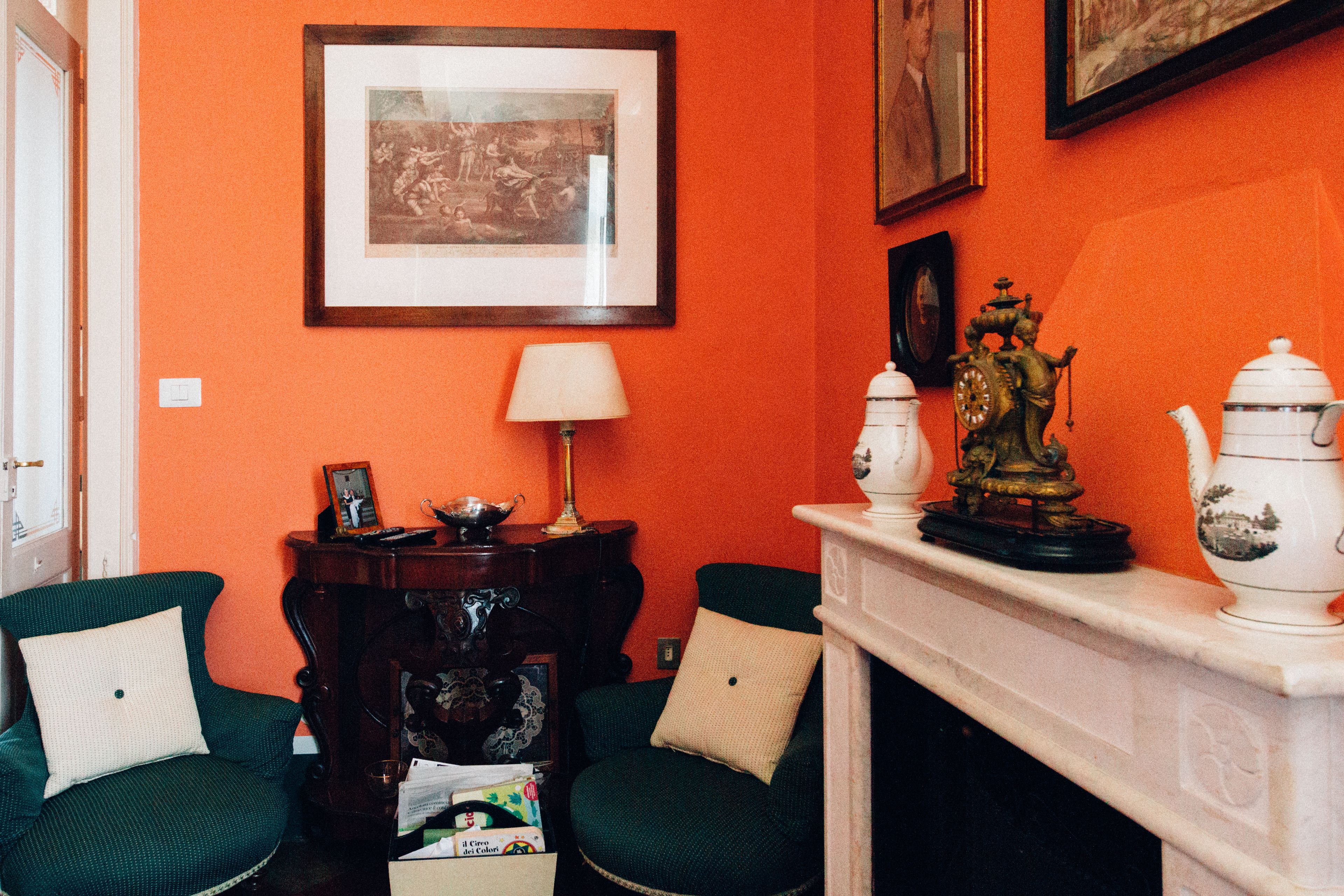 A room with two green armchairs, a fireplace with decorative items, and framed artwork on the wall.