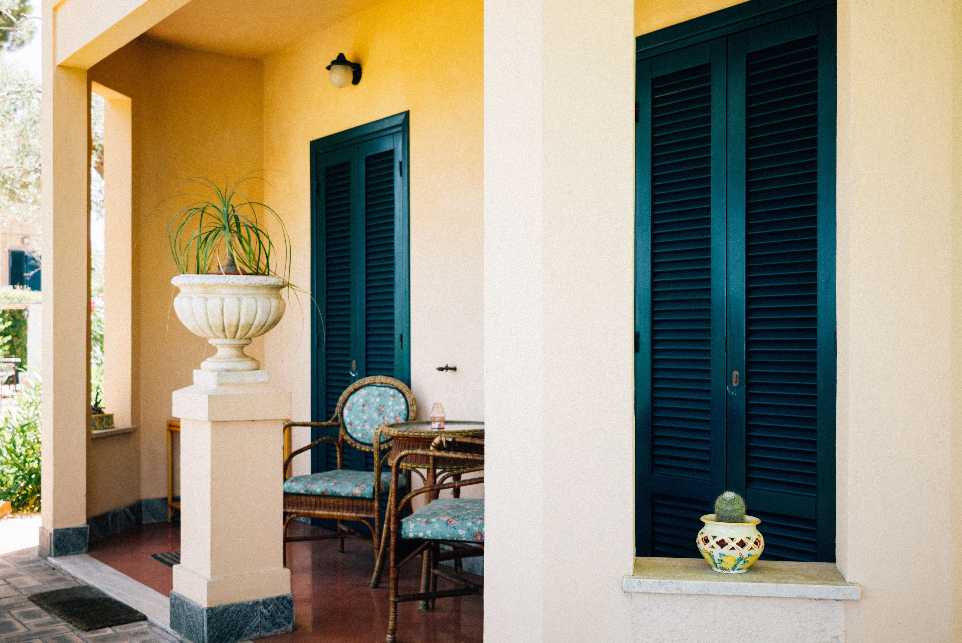 A patio with a table and chairs, a potted plant, and a window with a shutter.