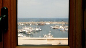 Vista de un puerto deportivo con varias embarcaciones amarradas, un muelle y un faro a lo lejos.