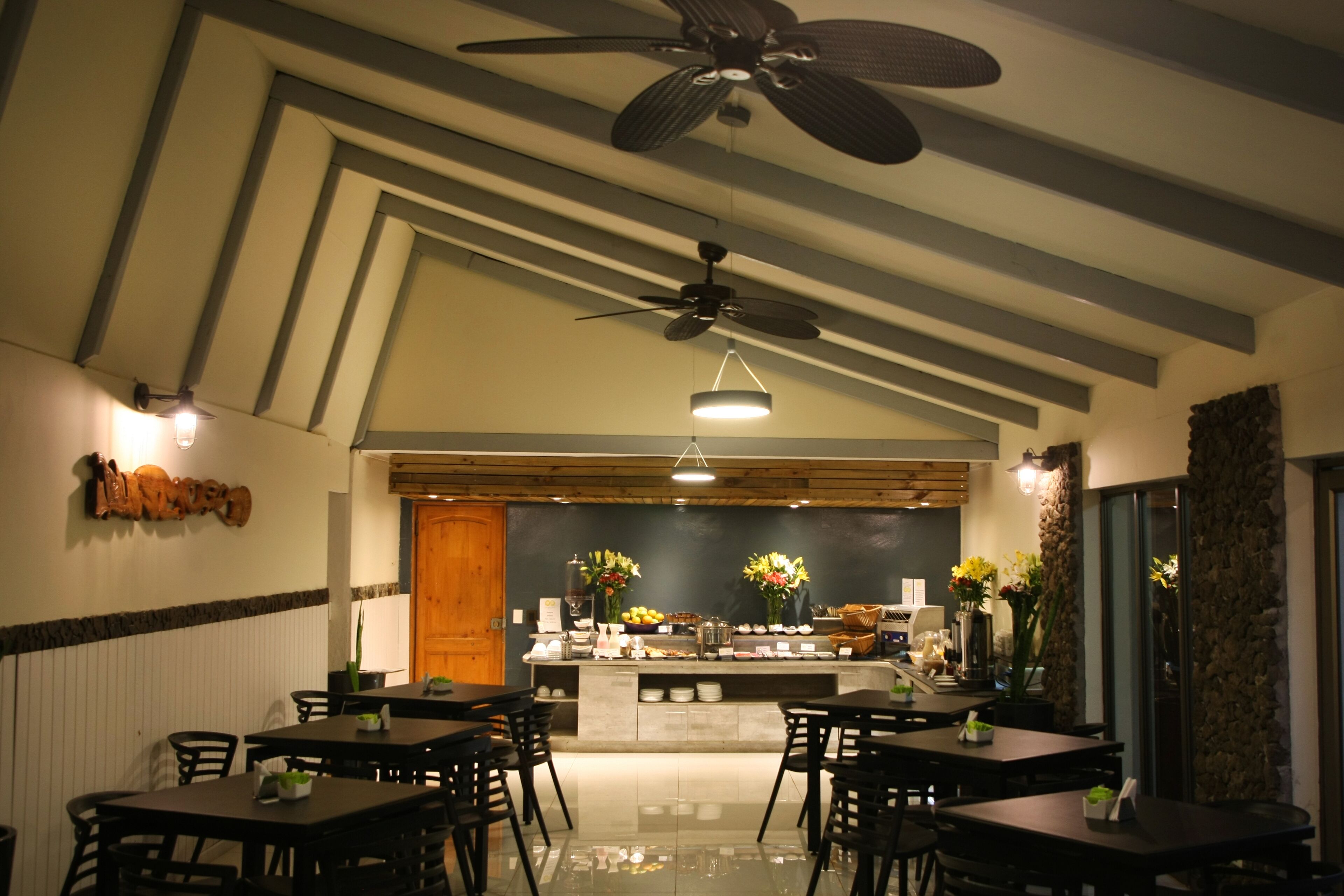 A restaurant with a modern interior, featuring a central counter with a display of fruits and flowers, surrounded by tables and chairs.