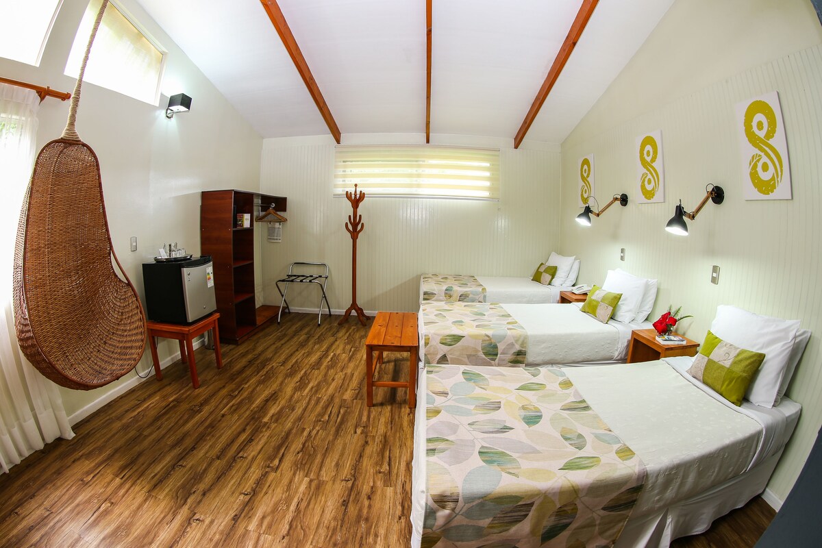 A room with two beds, a wooden floor, a wicker chair, a desk, and a wardrobe.