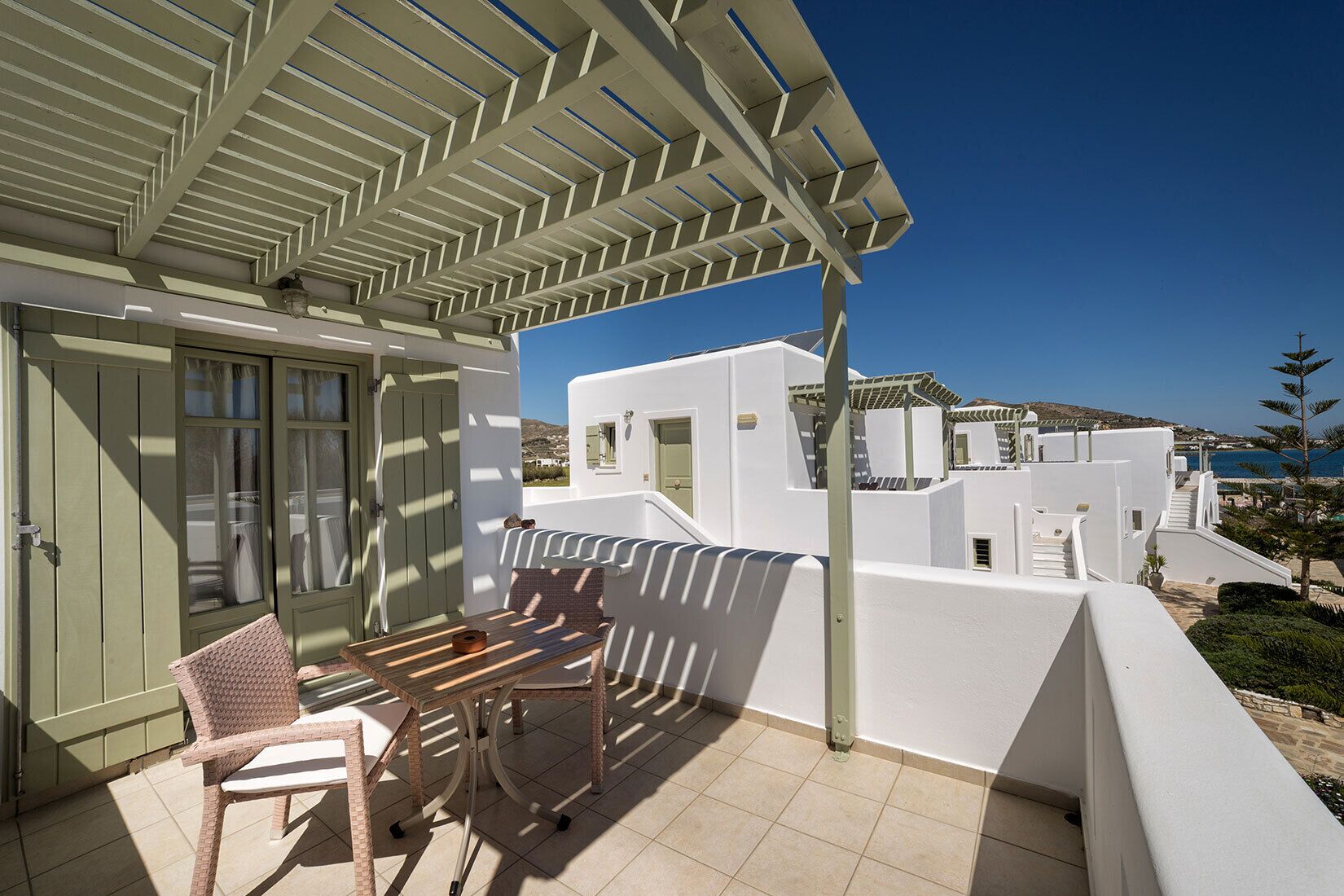 A balcony with a table and chairs, white walls, and a view of the sea and buildings.
