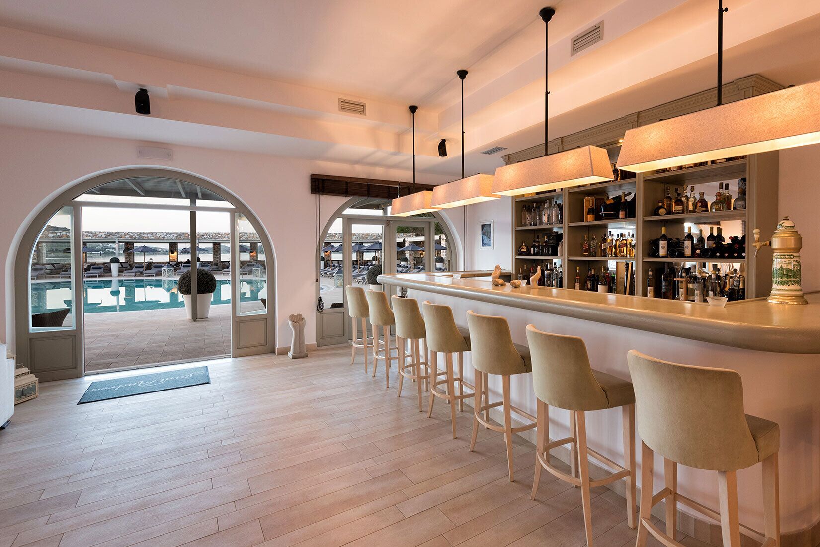 A bar area with a pool view, wooden flooring, and bar stools.