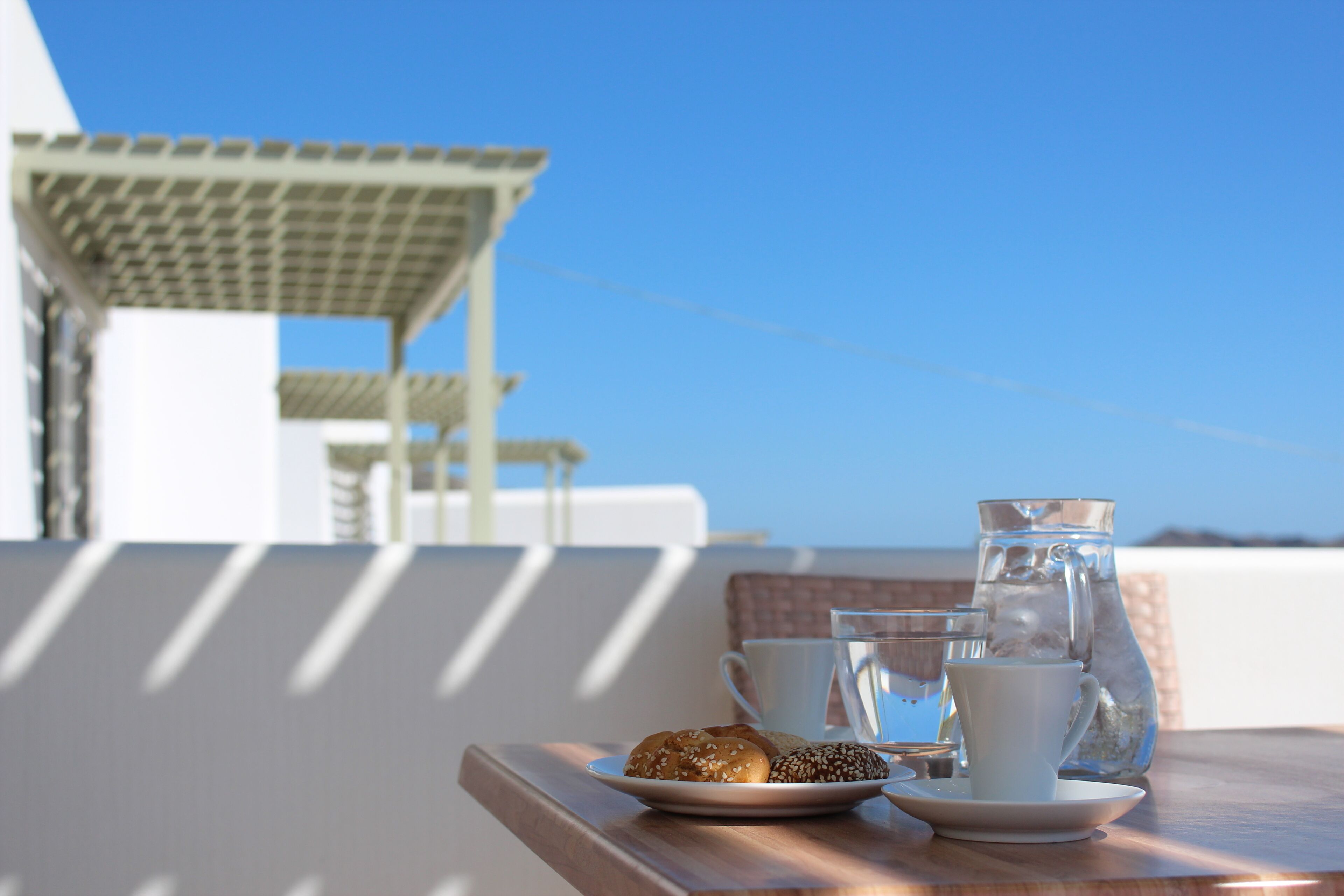 A table with a plate of pastries, a pitcher, and two cups on a balcony overlooking a clear sky.