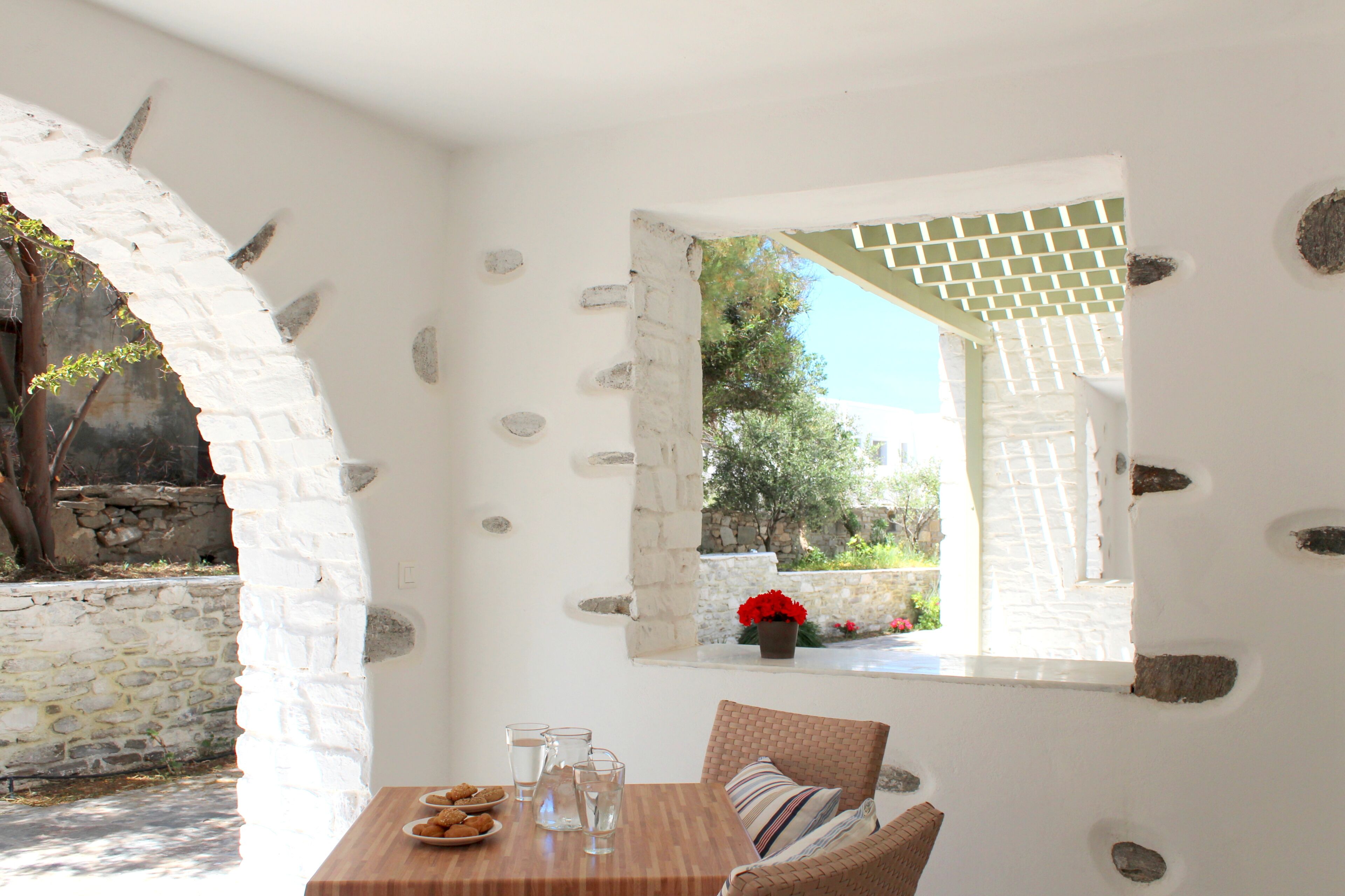 Una habitación con pared de piedra, una mesa de madera con un plato de galletas, vasos y una silla de mimbre.