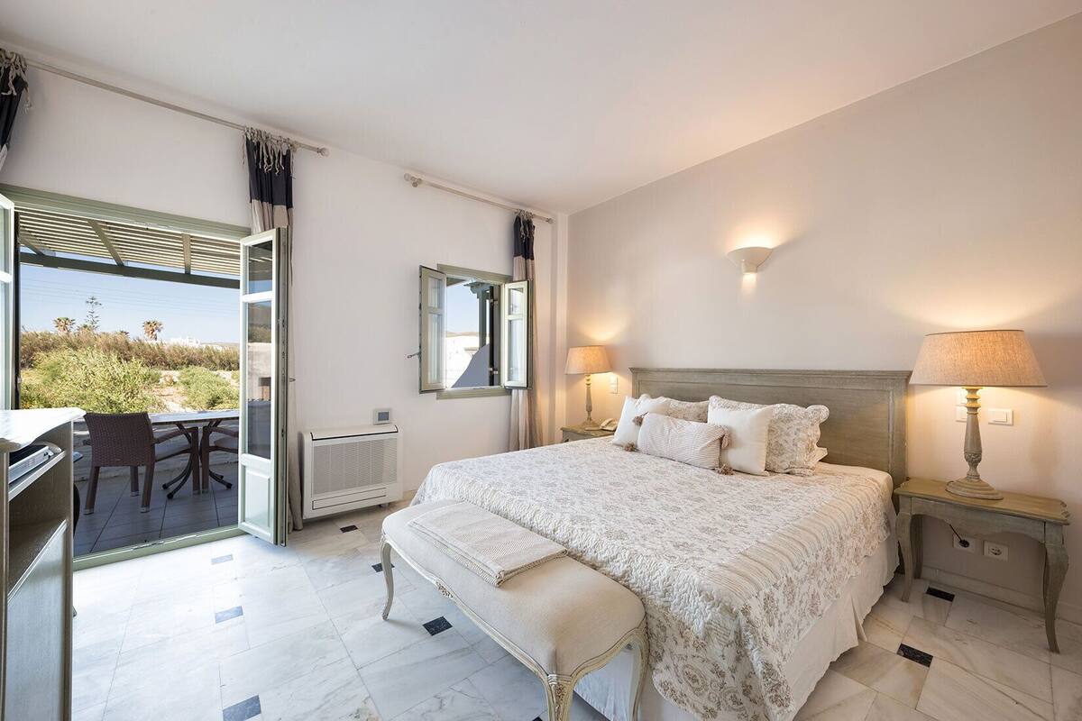Un dormitorio con una cama grande, un escritorio con silla, una ventana con cortinas y vistas al exterior.