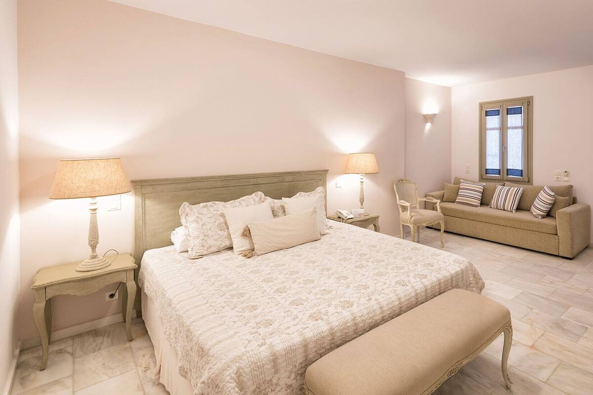 Un dormitorio con una cama grande, dos mesitas de noche, una silla, un sofá y una ventana.