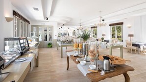 A spacious hotel dining area with a buffet setup, a coffee station, and a view of the garden through large windows. - Saint Andrea Sea Side Resort - Adults Only (Paros)