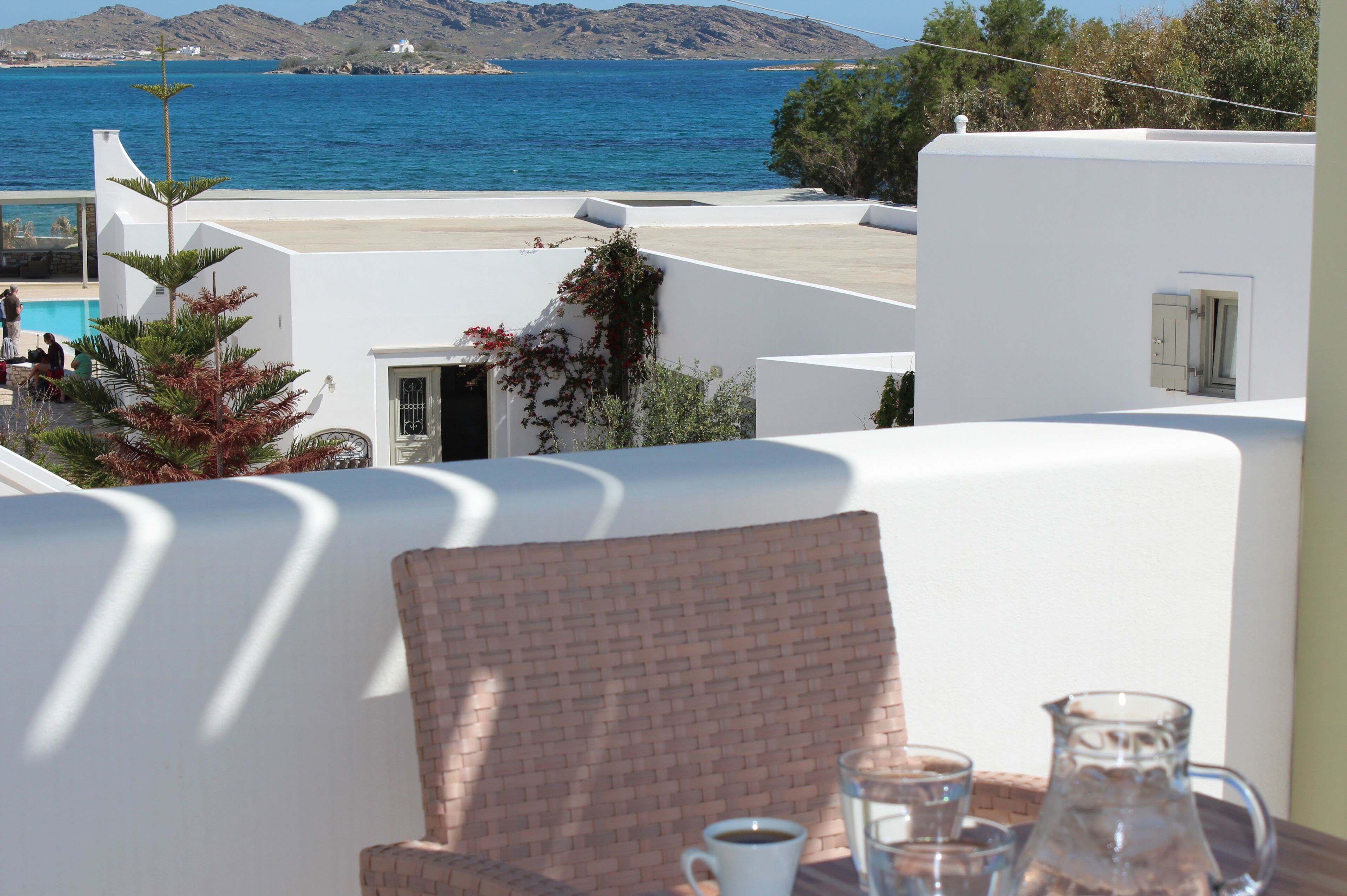 Una terraza con vistas al mar, edificios blancos y una mesa con una jarrón y una taza.
