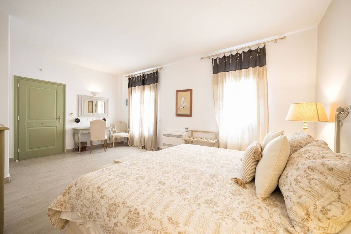 Un dormitorio con una cama grande, un escritorio, una silla, un espejo y una ventana con cortinas.