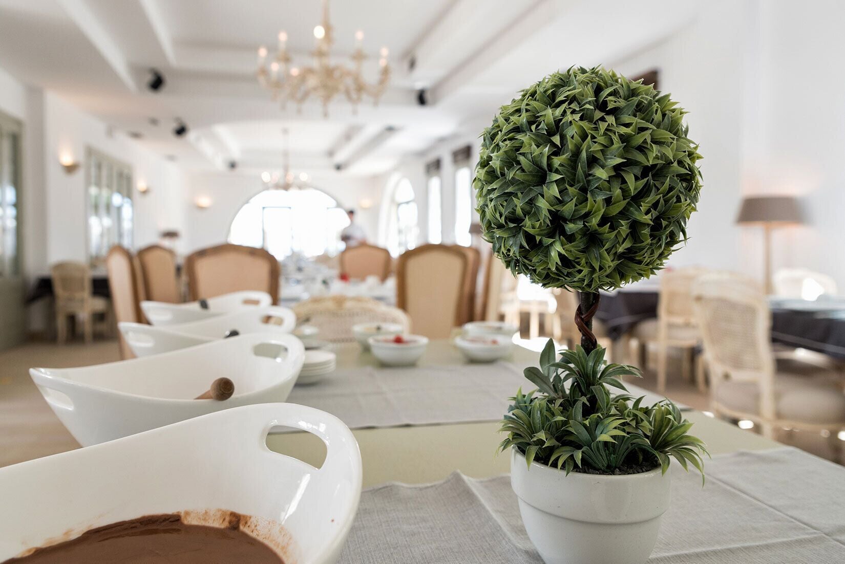 A dining area with white tableware, a potted plant, and a chandelier.