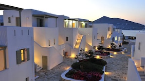 A white-washed building with a stone-paved courtyard, featuring a central garden with flowers and a staircase leading to the upper floors. - Saint Andrea Sea Side Resort - Adults Only (Paros)