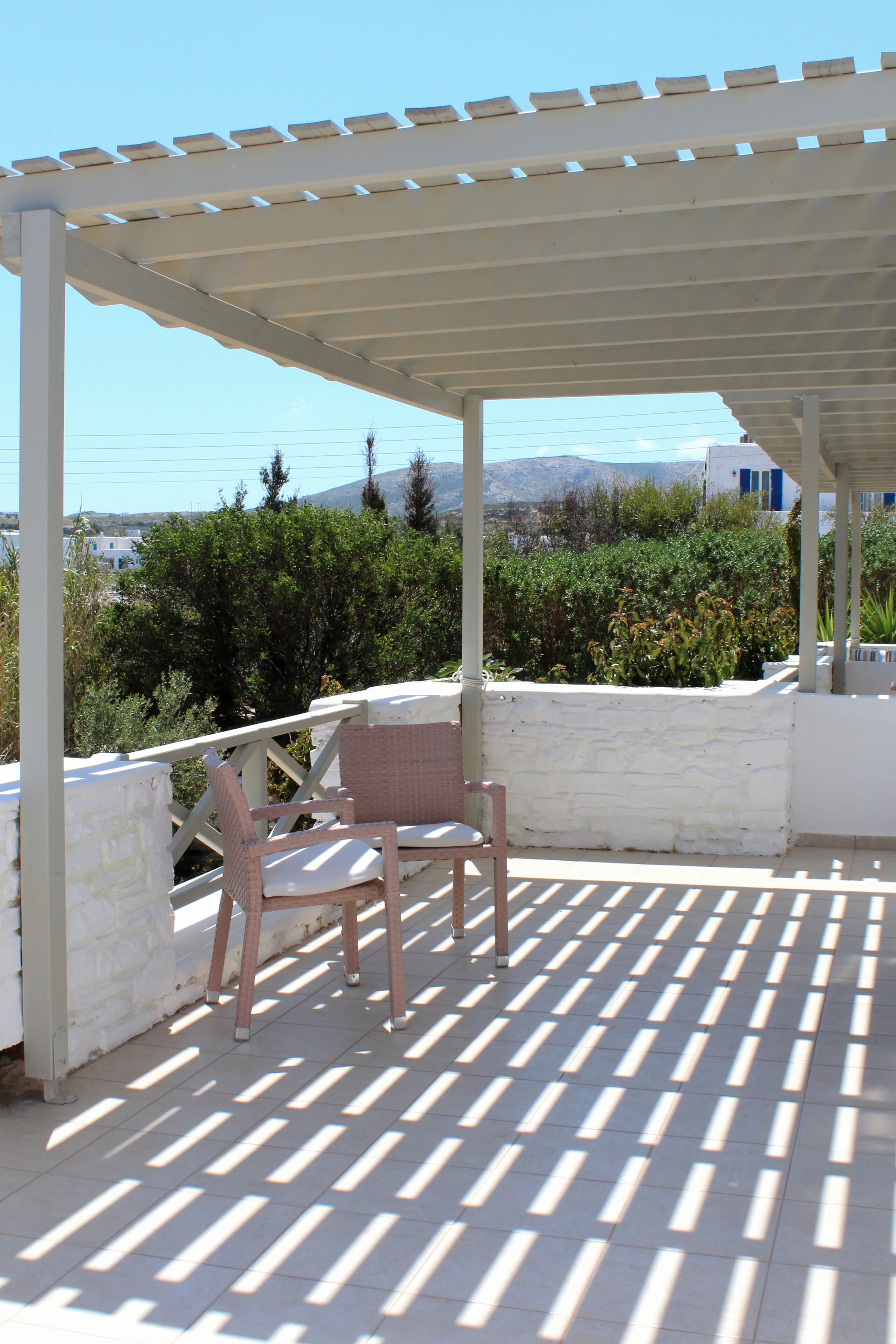 A covered outdoor seating area with a pergola, a stone wall, and a view of the landscape.