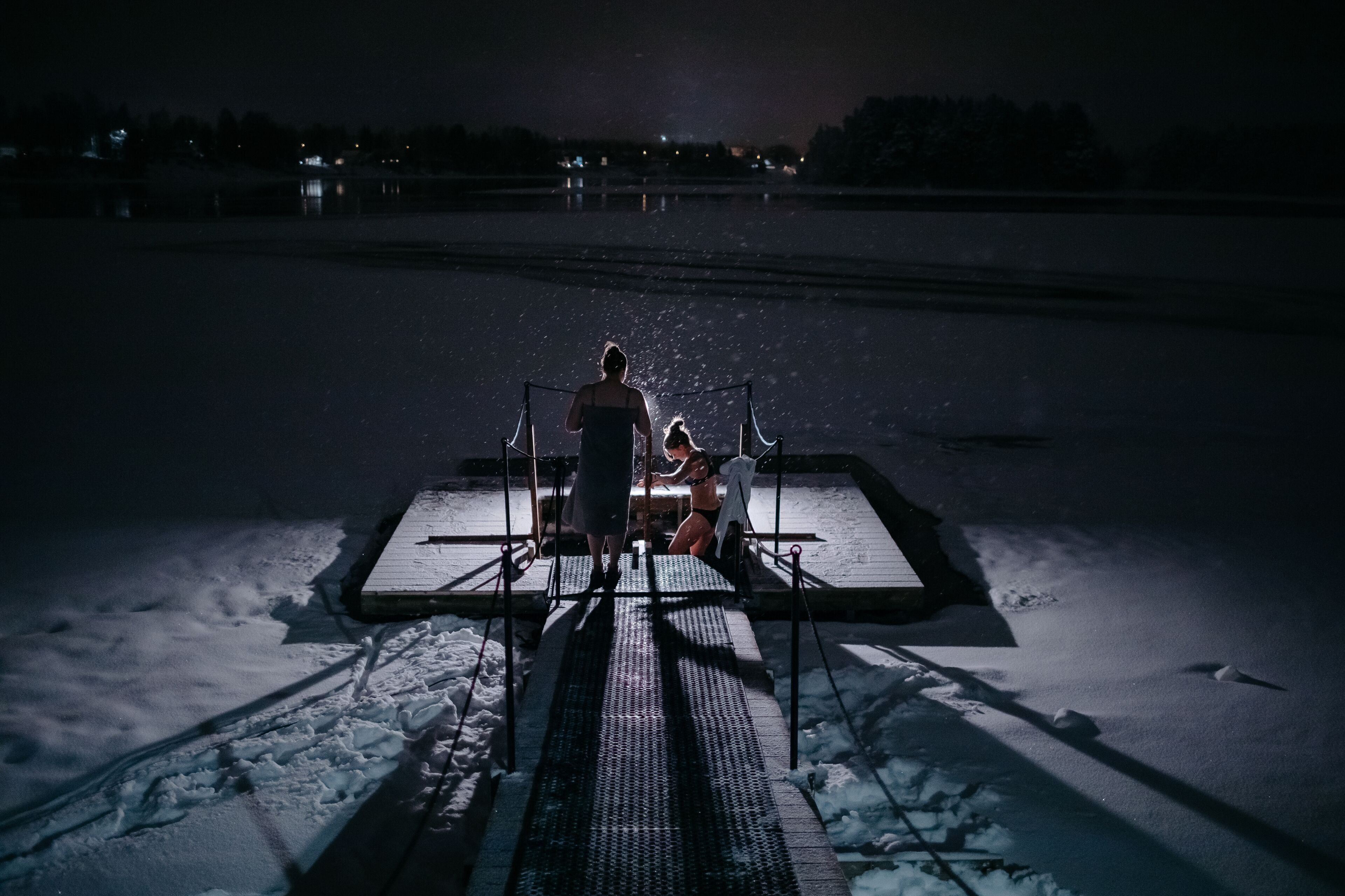 A person standing on a platform with a child, overlooking a snowy landscape at night.