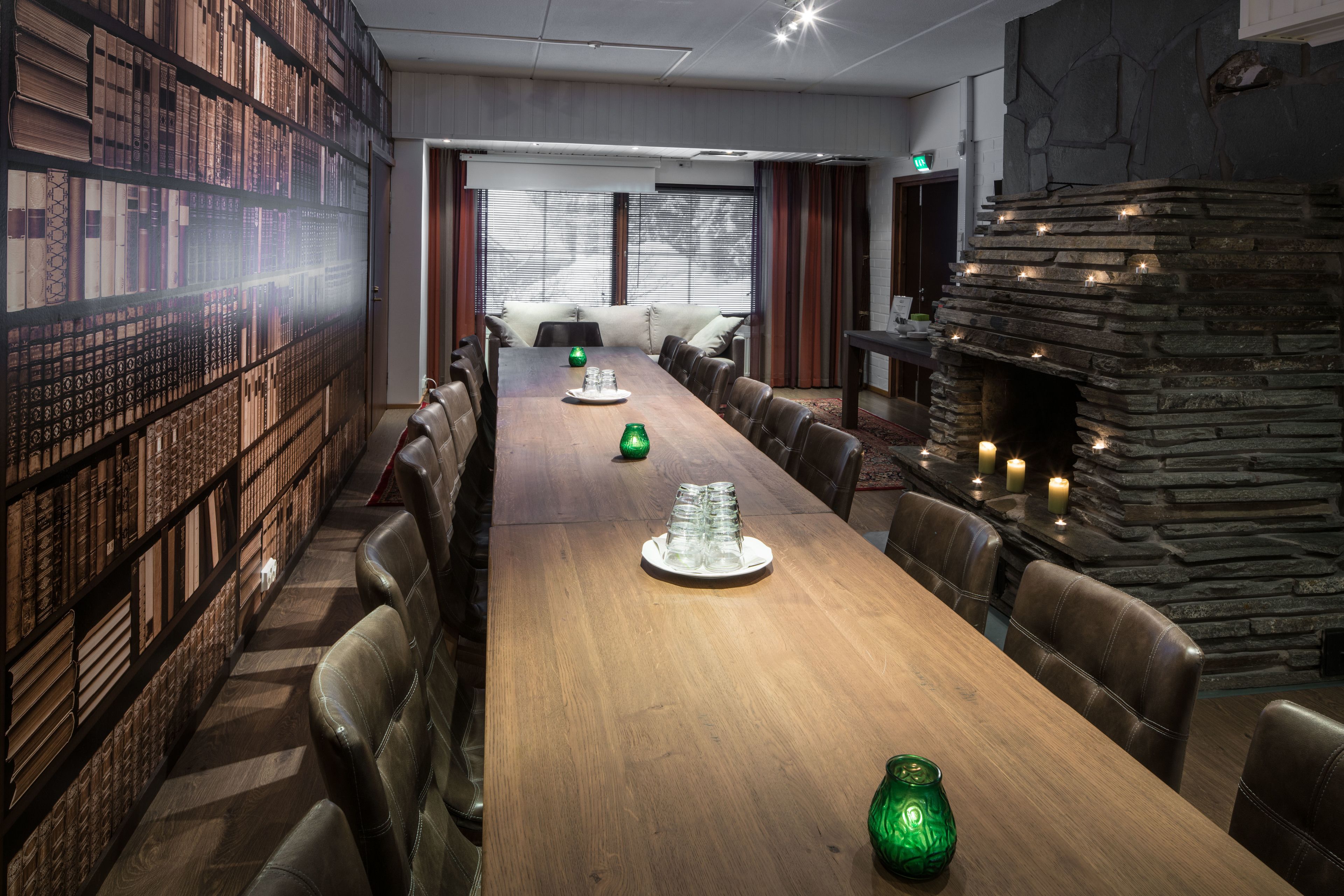 A long wooden table with chairs, a bookshelf, and a stone fireplace.