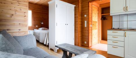 Un acogedor interior de cabaña de madera con un sofá gris, una mesa de comedor de madera, un armario blanco y una zona de cocina.