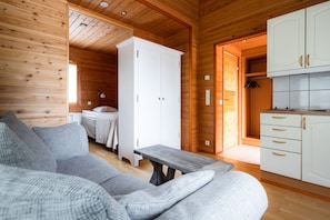 Ein Holzblockhaus-Interieur mit einer Couch, einem Bett, einem weißen Schrank und einer Küchenzeile.