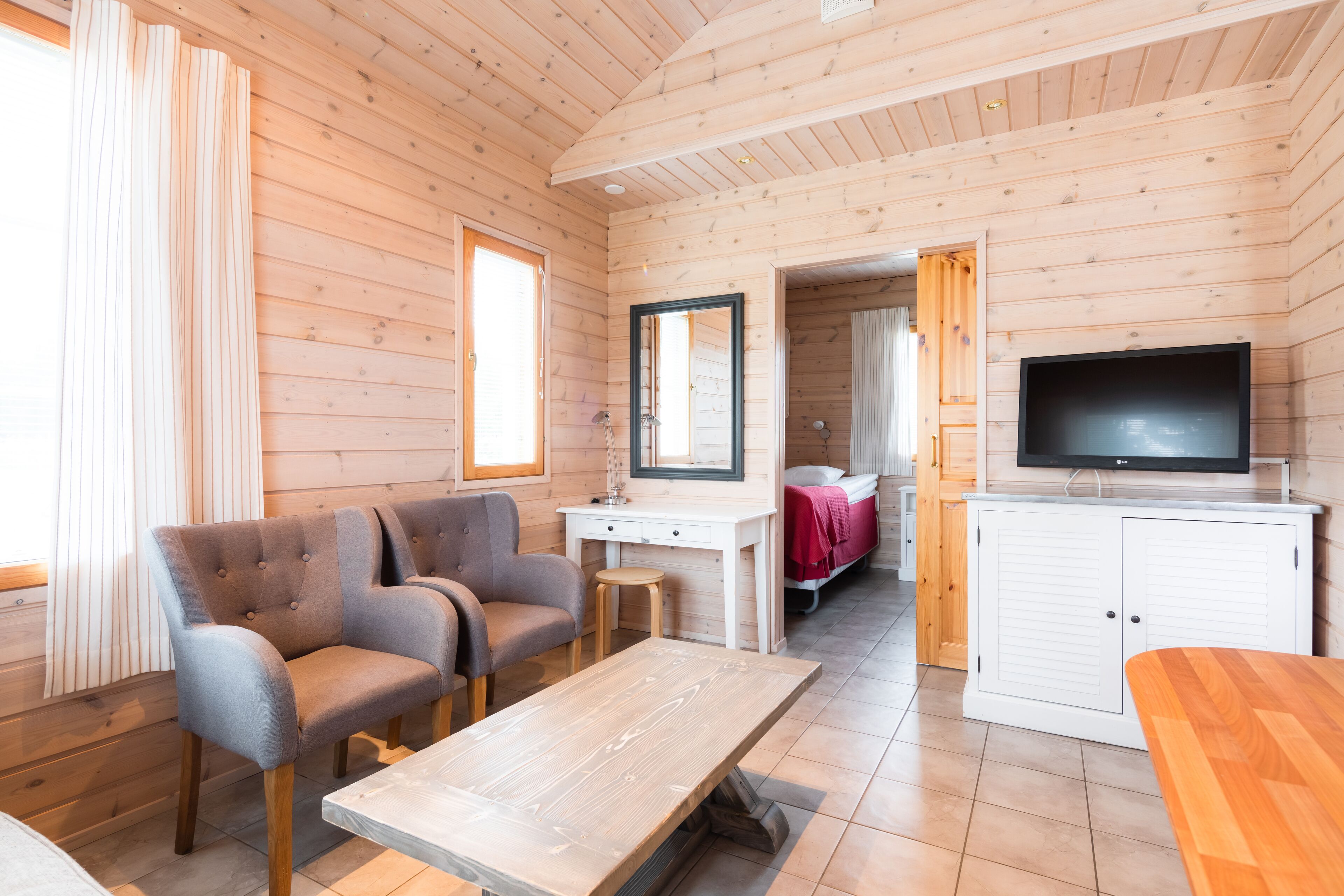 Interior de una cabaña de madera con sofá, televisor, mesa de madera y un baño visible a través de una puerta abierta.