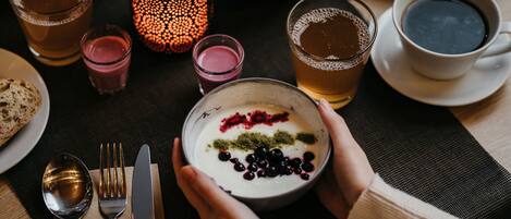 A table with a bowl of yogurt topped with berries and a candle, surrounded by various beverages and plates.