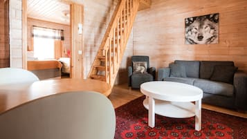 A wooden interior with a staircase, a gray sofa, a white table, and a red patterned rug.