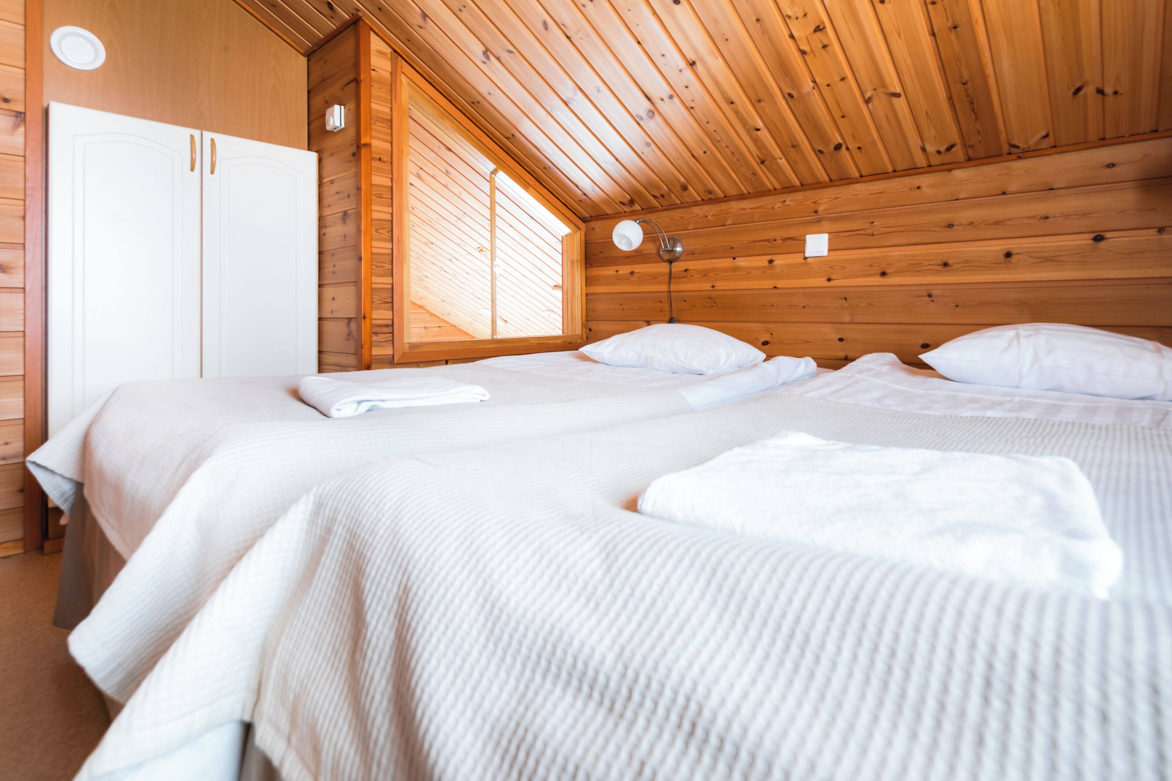 Ein Schlafzimmer mit Holzbalkendecke, einem großen Bett mit weißer Bettwäsche, einem Kleiderschrank und einem Fenster mit Jalousien.