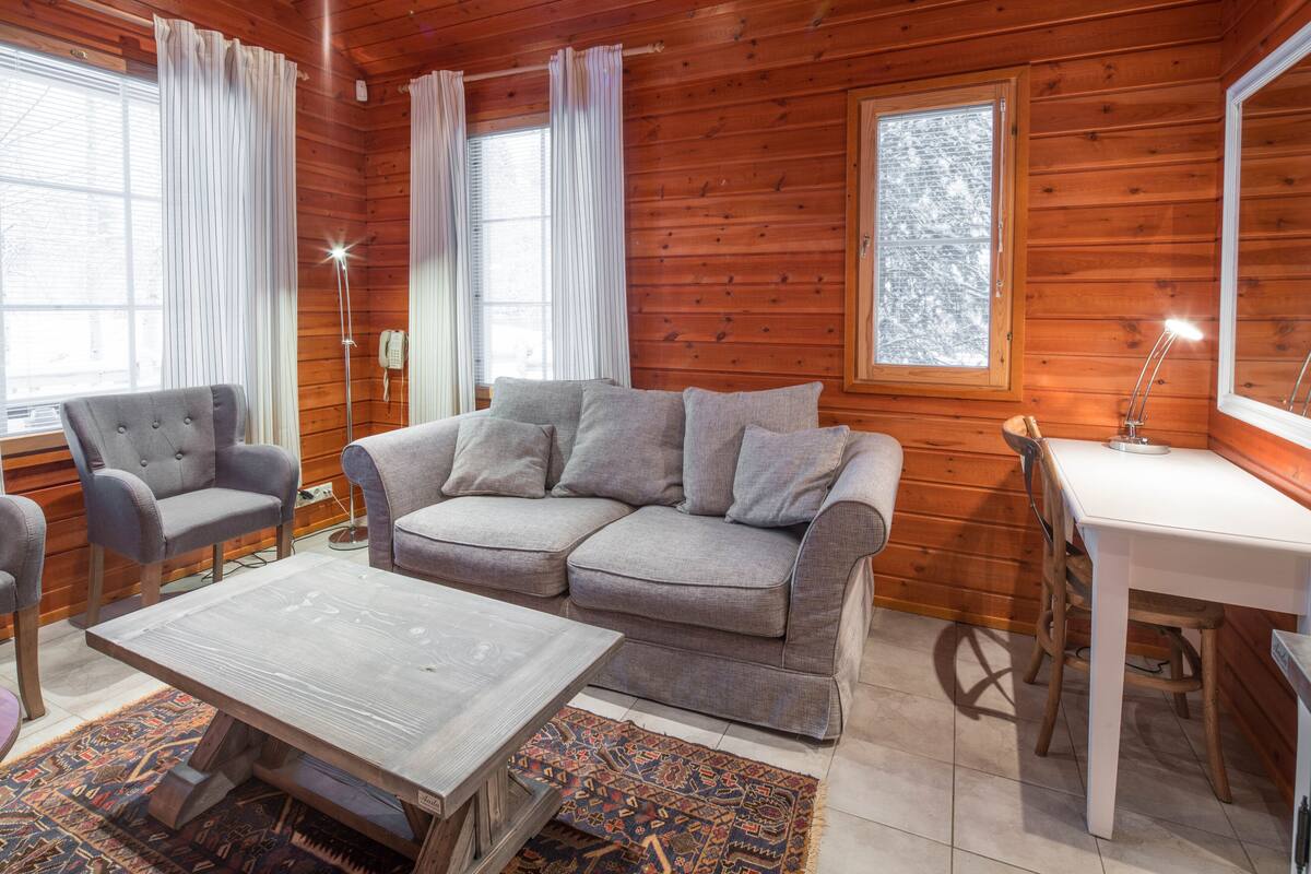 Una habitación acogedora con un sofá gris, una mesa de centro de madera y un escritorio blanco.