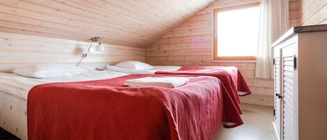 A cozy cabin room with two beds, a wooden ceiling, a window with curtains, and a wardrobe.