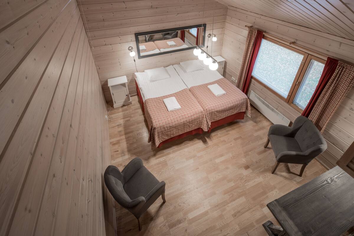 Un dormitorio de cabaña de madera con una cama grande, dos mesitas de noche, una silla y una pequeña mesa.