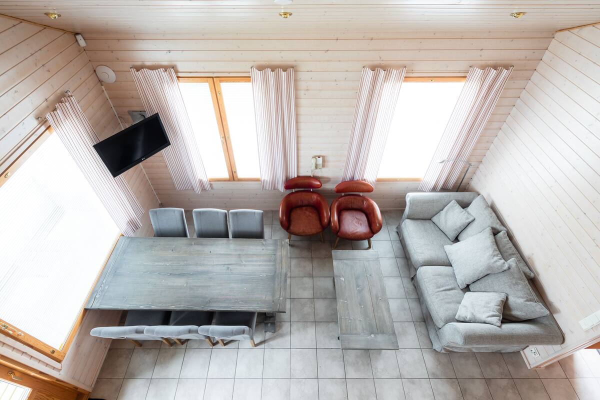 Una habitación con techo de madera, un sofá gris, otro sofá gris y una mesa de comedor con sillas.