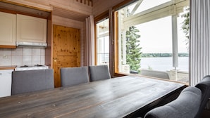 Ein Holzinterieur mit einem Esstisch und Stühlen, einer Küchenzeile und großen Fenstern mit Blick auf ein Gewässer.