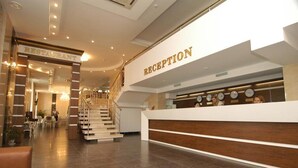 Een hotel receptie met een trap naar de verdieping erboven, een receptiebalie en een bord met daarop een restaurant.