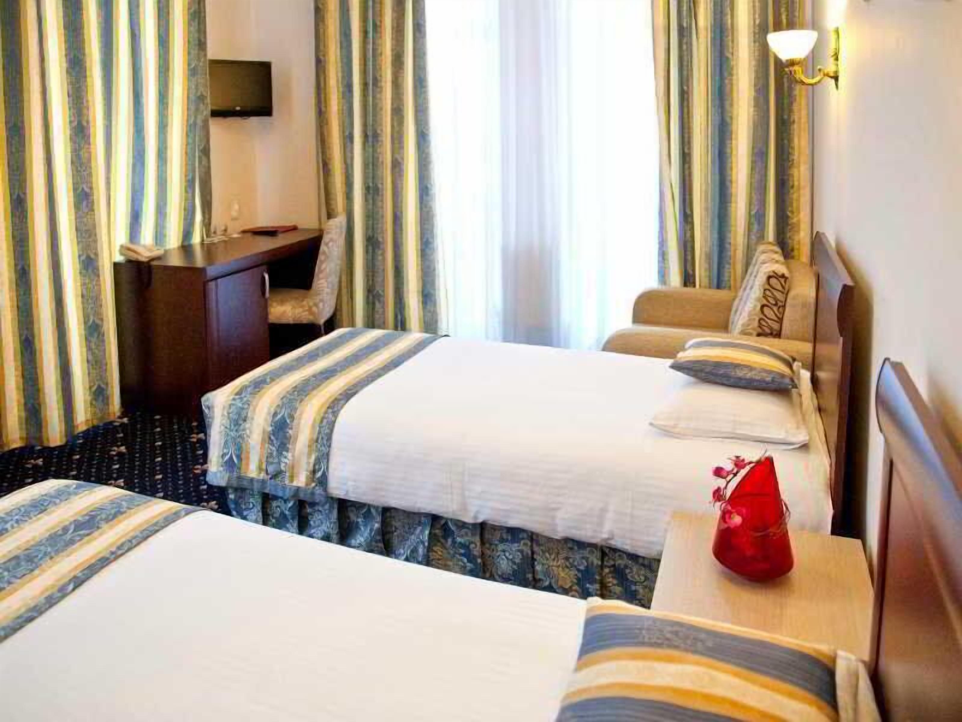 A hotel room with two beds, a desk, a TV, and a lamp.