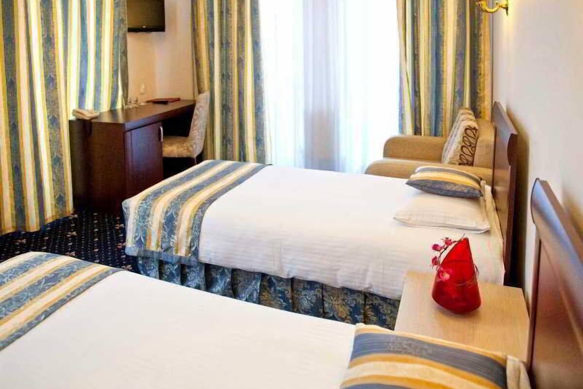 A hotel room with two beds, a desk, a chair, a TV, and a window with curtains.